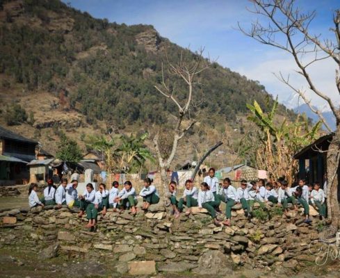 Kinder sitzen auf Steinmauer in Swaragau