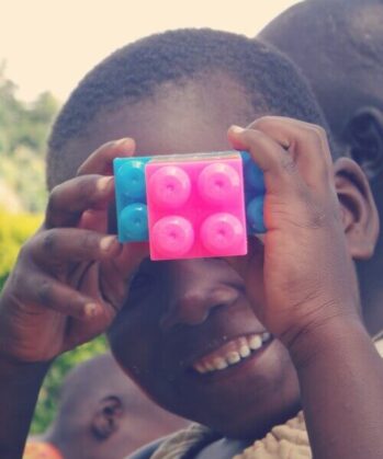 Kind hält sich einen blauen und einen rosaroten Legostein vor das Gesicht