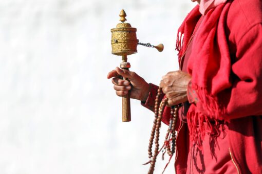 Mönch hält Gebetsmühle und Mala in der Hand