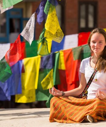 Mädchen meditiert in Nepal und ist von Gebetsfahnen umgeben