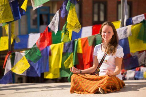 Mädchen meditiert in Nepal und ist von Gebetsfahnen umgeben