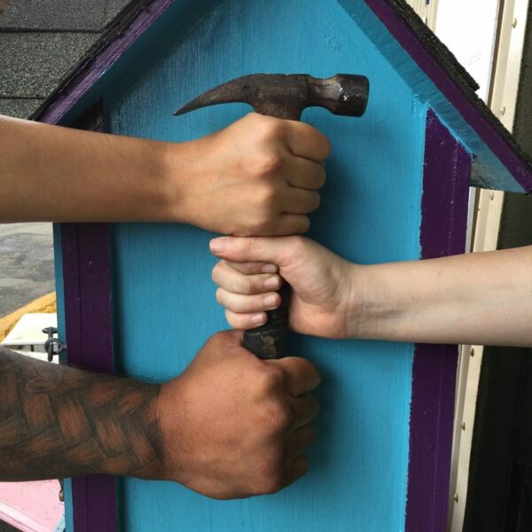 Drei Volunteer-Hände umfassen Hammer